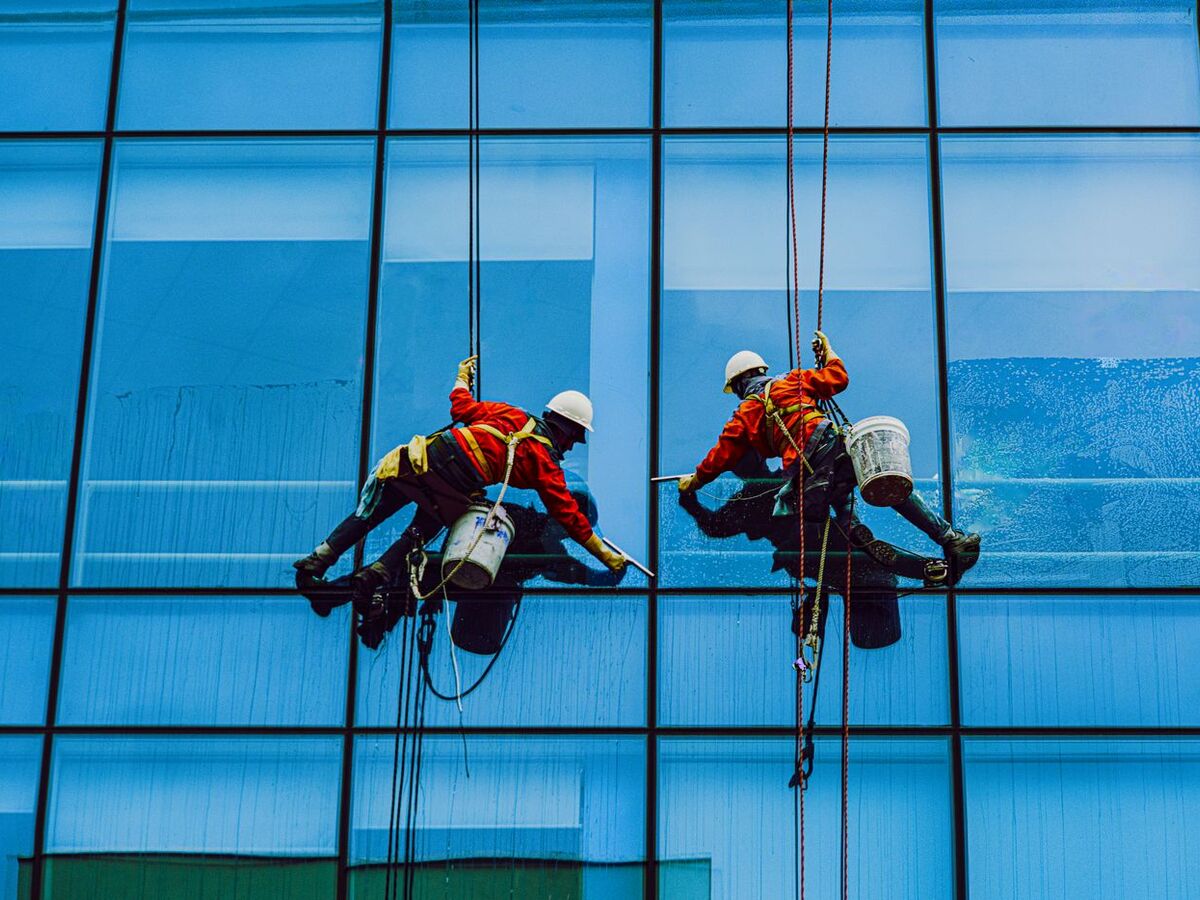 Window cleaners on ropes cleaning a blue glass office facade